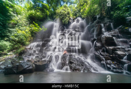 Frau sitzt auf Felsen, Wasserfall, Luft Terjun Kanto Lampo, in der Nähe von Ubud, Bali, Indonesien Stockfoto