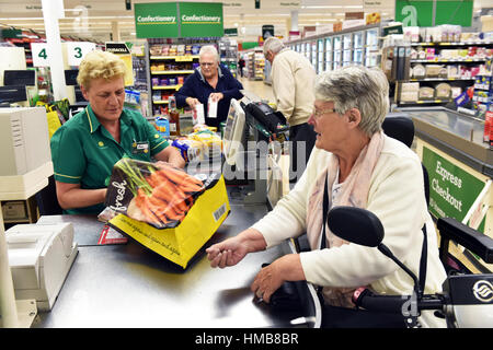 Eine behinderte Frau wird an der Supermarktkasse mit ihren Einkaufsmöglichkeiten, Tasche packen geholfen. Stockfoto