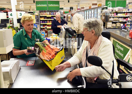 Eine behinderte Frau wird an der Supermarktkasse mit ihren Einkaufsmöglichkeiten, Tasche packen geholfen. Stockfoto