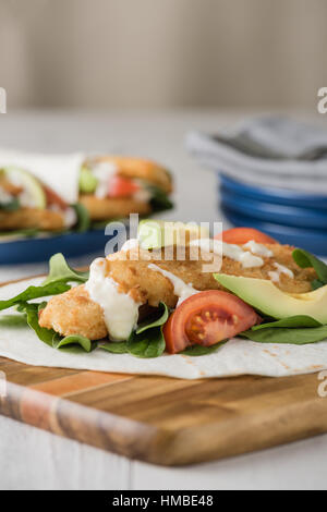 Fisch-Finger wickelt mit Avocado und Tomaten serviert auf hölzernen Käseplatte Stockfoto