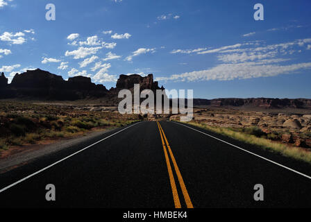 Kurvenreiche schwarze Asphaltstraße verschwindet in der Ferne in Utah im Sommer, an einem klaren Tag aufgenommen. Felsige Umrisse im Hintergrund. Stockfoto