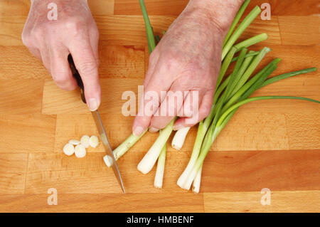 Nahaufnahme von ein paar Hände schneiden Salat Zwiebeln auf ein Schneidbrett aus Holz Stockfoto