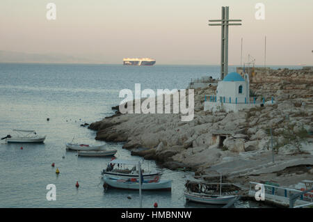 Agios Nikolaos-Kapelle, Frachtschiff und kleine Boote in einem Strand südlich von Athen, Piräus, Griechenland Stockfoto