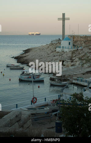 Agios Nikolaos-Kapelle, Frachtschiff und kleine Boote in einem Strand südlich von Athen, Piräus, Griechenland Stockfoto