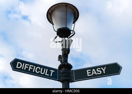 Straßenbeleuchtung-Stock mit zwei gegenüberliegenden Richtungspfeile auf blauem Hintergrund bewölkt. Schwierig im Vergleich zu einfachen Konzept. Stockfoto