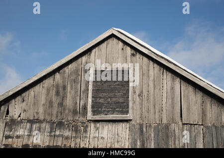 Blauer Himmel und Sonnenschein für diese alten Farm Gebäude mit verwitterten grau und schwarz lackierten Scheune Board. Eine alte Tür oder ein Fenster ist auf der Seite eingerahmt. Und wo Stockfoto