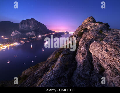 Blick vom Gipfel auf die nächtliche Stadt, blaues Meer und hohen Felsen gegen schönen Himmel. Nachtlandschaft bunten Berg Stockfoto