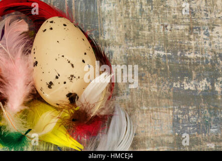 Großes gesprenkelten Ei in einem Nest aus gefärbten Federn auf alten Holztisch mit textfreiraum auf der rechten Seite. Enge, horizontale, flache Ansicht. Stockfoto