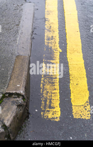 Doppelte gelbe Linien auf einer nassen Straße neben einem Bordstein mit Textfreiraum. Stockfoto