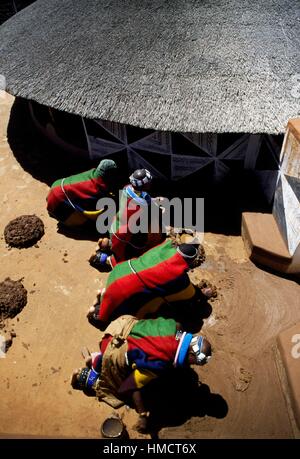 Männer absetzen Bodenbelag vor ein Rondavel (runden oder ovalen Traditionshaus) in einem Ndebele Dorf, Südafrika. Stockfoto