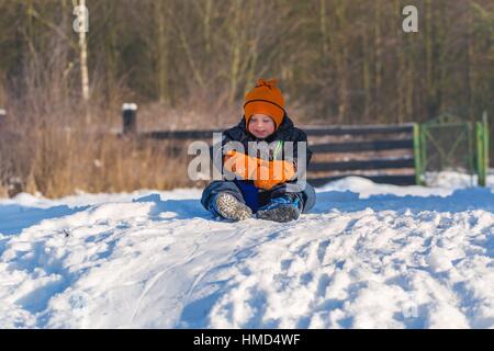 Glückliche kleine kaukasischen junge Abfahrt auf Kunststoff Schieber oder Schlitten. Winter Kind outdoor-Aktivität. Stockfoto