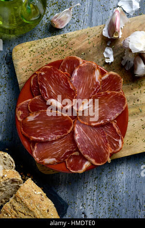 High-Angle Shot einer Platte mit einigen Scheiben von spanischen Lomo Embuchado, ausgehärteten Schweinefilet, einige Scheiben Brot, ein Glas Menage mit Olivenöl und s Stockfoto