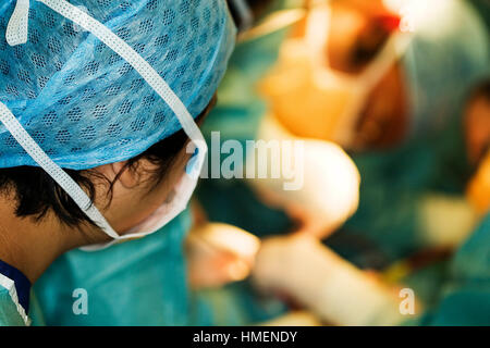 Mischlinge NHS-OP-Schwester, Uhren auf als Chirurg im Theater in Großbritannien NHS Krankenhaus Operation durchführt Stockfoto