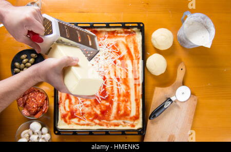 Mann reiben Käse auf einem Pizzateig. Pizza backen Stockfoto