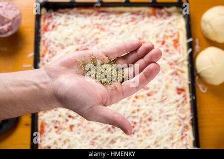 Hand mit Oregano über Pizza in Herstellung Stockfoto