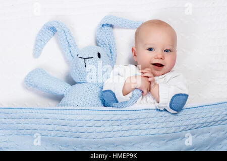 Lustige kleine Baby tragen eine warme Strickjacke, spielen mit Spielzeug Hase auf weißem Kabel stricken Decke im sonnigen Kindergarten Stockfoto