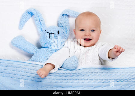 Lustige kleine Baby tragen eine warme Strickjacke, spielen mit Spielzeug Hase auf weißem Kabel stricken Decke im sonnigen Kindergarten Stockfoto