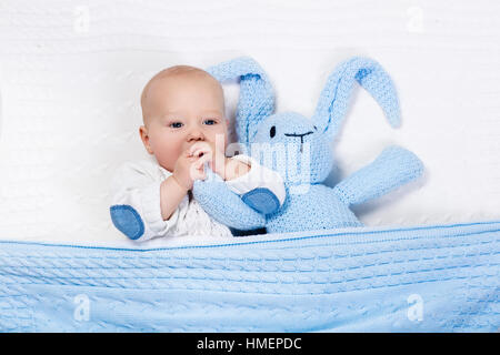 Lustige kleine Baby tragen eine warme Strickjacke, spielen mit Spielzeug Hase auf weißem Kabel stricken Decke im sonnigen Kindergarten Stockfoto