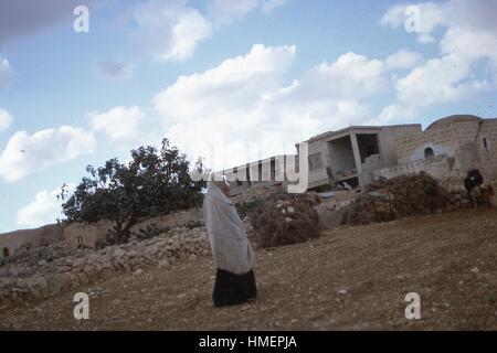 Arabische Frau trägt einen Niqab oder Burka trägt ein Kind während des Gehens über felsigen Boden in Richtung Häusern und Gebäuden im Hintergrund, in Hebron, Israel, November 1967. (Foto von Morse Sammlung/Gado/Getty Images). Stockfoto