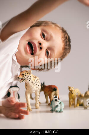 Ein vier Jahre alter Junge spielt mit verschiedenen Tiermodellen auf einem Tisch Stockfoto