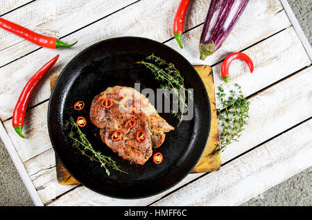 Fleisch mit Gewürzen in einer Pfanne, Rosmarin und hot Chili Peppers auf einem weißen Holztisch Hintergrund Stockfoto