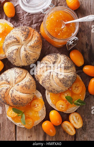 Kumquat-Marmelade in ein Glas Jar und süße Brötchen Nahaufnahme auf dem Tisch. vertikale Ansicht von oben Stockfoto