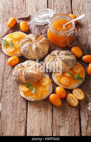 Kumquat-Marmelade in ein Glas Jar und süße Brötchen Nahaufnahme auf dem Tisch. Vertikal Stockfoto