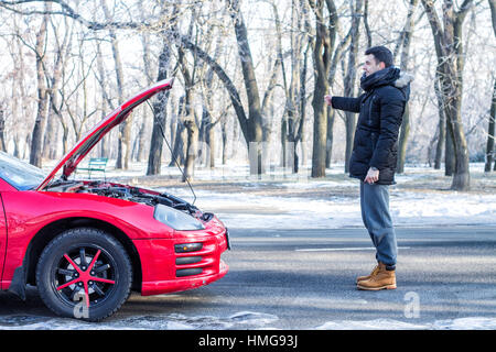 Mann Probleme mit gebrochenen Sportwagen auf Winterdienst-Signalisierung. Stockfoto