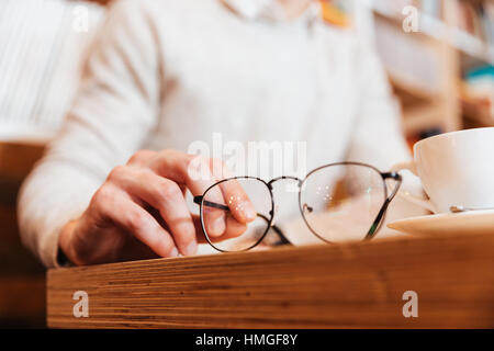 Bild des jungen Mannes im Café sitzen abgeschnitten. Hände halten Brillen im Mittelpunkt. Stockfoto