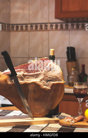 Spanischen Jamon Serrano auf hölzernen Tabla Jamonera mit Messer, Apfel, Glas und Flasche Rotwein. Kochen, Essen Foto Wohnkonzept Stockfoto