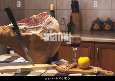 Spanischen Jamon Serrano auf hölzernen Tabla Jamonera mit Messer, Apfel, Glas und Flasche Rotwein. Kochen, Essen Foto Wohnkonzept Stockfoto