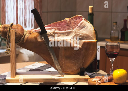 Spanischen Jamon Serrano auf hölzernen Tabla Jamonera mit Messer, Apfel, Glas und Flasche Rotwein. Kochen, Essen Foto Wohnkonzept Stockfoto