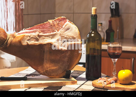 Spanischen Jamon Serrano auf hölzernen Tabla Jamonera mit Messer, Apfel, Glas und Flasche Rotwein. Kochen, Essen Foto Wohnkonzept Stockfoto