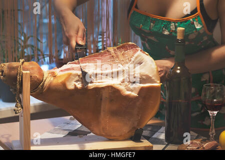 Frau Hände Slises spanischen Jamon Serrano auf hölzernen Tabla Jamonera. Flasche und Glas Rotwein. Selektiven Fokus. Kochen, Essen Foto Wohnkonzept. Stockfoto