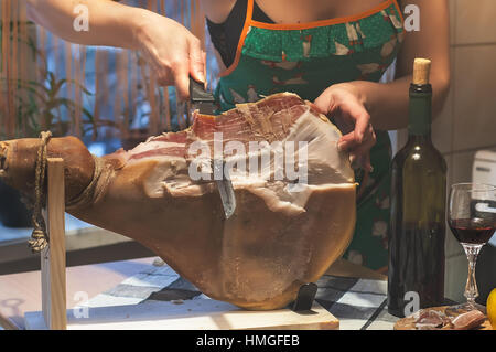 Frau Hände Slises spanischen Jamon Serrano auf hölzernen Tabla Jamonera. Flasche und Glas Rotwein. Selektiven Fokus. Kochen, Essen Foto Wohnkonzept. Stockfoto