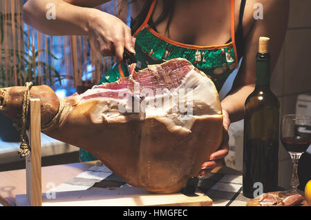 Frau Hände Slises spanischen Jamon Serrano auf hölzernen Tabla Jamonera. Flasche und Glas Rotwein. Selektiven Fokus. Kochen, Essen Foto Wohnkonzept. Stockfoto