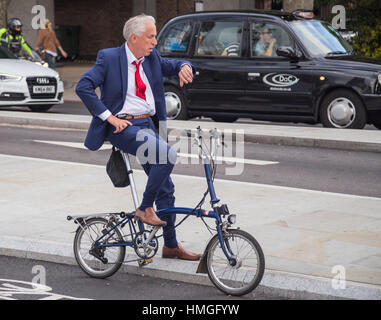 gut gekleideter Mann im blauen Anzug auf Klapp Fahrrad warten an der Ampel auf der Nord-Süd-Zyklus Superhigheway (CS6) auf Blackfriars Road, London SE1 Stockfoto