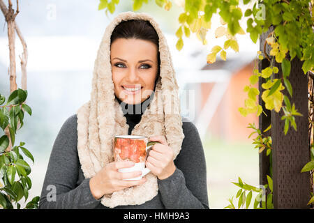 Schöne grüne Augen junge Frau in warme Kleidung und Beige Schal Lächeln, halten eine Tasse Tee im Freien, im Herbst Stockfoto