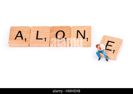 Scrabble Buchstaben bilden das Wort allein. Ein junger Mann sitzt auf der Buchstabe E des Wortes allein. Stockfoto