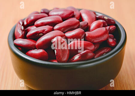 Trockene rote Kidney-Bohnen in schwarz Schüssel und auf Holztisch Stockfoto