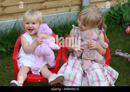 Kleine blonde Mädchen, Kinder Kinder sitzen Garten Stuhl aus Kunststoff, zusammen zu spielen, umarmen, kuscheln Teddys Teddys Konzept, das Glück ist reine Freude Stockfoto