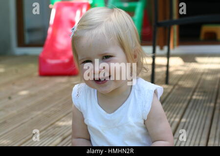 Blonde Mädchen / Kleinkind Zahnen, zwei unteren Zähne, lächelnd im Garten tragen ein weißes T-Shirt, süße blonde Baby lachen, neue Zähne glücklich Stockfoto