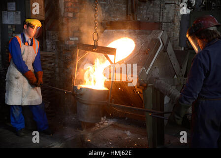 Gießer geschmolzenes Eisen aus einem Induktionsofen in der Ladel in einer kleinen Gießerei gießen. (Bei vorhandenem Licht mit geringen Schärfentiefe erschossen Sie.) Stockfoto