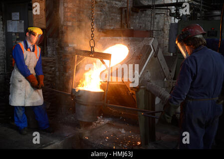 Gießer geschmolzenes Eisen aus einem Induktionsofen in der Ladel in einer kleinen Gießerei gießen. (Bei vorhandenem Licht mit geringen Schärfentiefe erschossen Sie.) Stockfoto