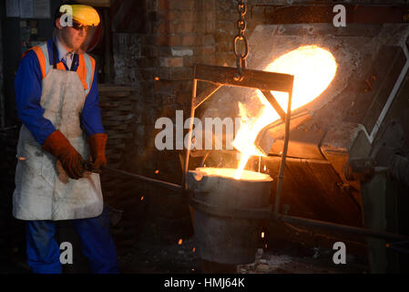 Gießer geschmolzenes Eisen aus einem Induktionsofen in der Ladel in einer kleinen Gießerei gießen. (Bei vorhandenem Licht mit geringen Schärfentiefe erschossen Sie.) Stockfoto