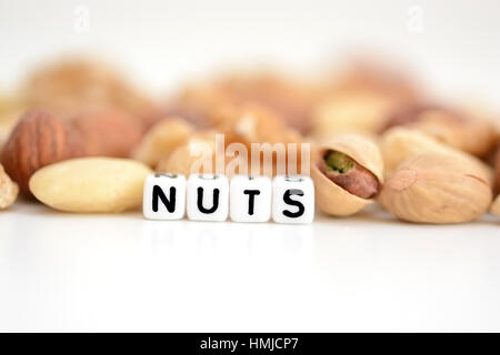 Rohe Nüsse und das Wort "Nuts" von Fliesen- buchstaben Perlen verteilt auf einem weißen Tisch geschrieben Stockfoto