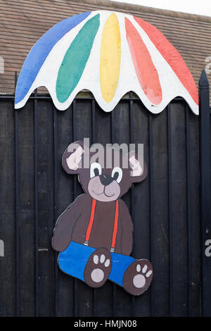 hölzerne ausgeschnittene Teddybär unter einem Regenbogen Regenschirm Stockfoto