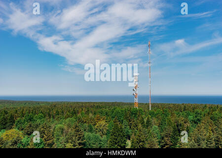 Telekommunikation-Türme mit TV-Antennen und Satellitenschüssel in Wald, blauer Himmel und Meer im Hintergrund Stockfoto