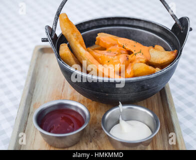 Pommes Frites mit Käse garniert. Soße und Mayonnaise auf einem Holztablett umfasst. Stockfoto