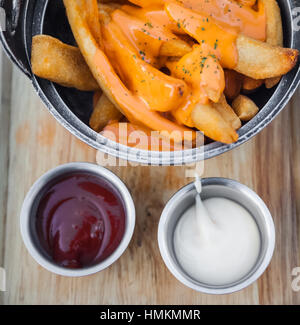 Pommes Frites mit Käse garniert. Soße und Mayonnaise auf einem Holztablett umfasst. Stockfoto